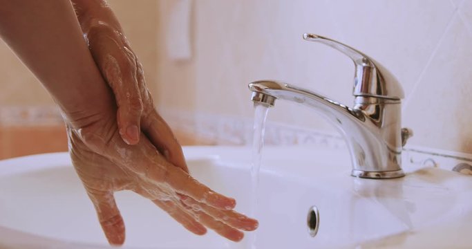 Woman carefully washing her hands with soap and water in bathroom. Detail of woman's hands washing on sink.Slow motion close-up