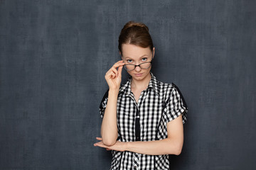 Portrait of serious focused young woman looking over glasses at you