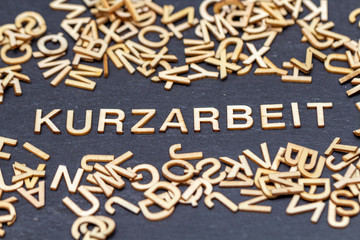 Text Kurzarbeit aus Holzbuchstaben auf Schieferplatte