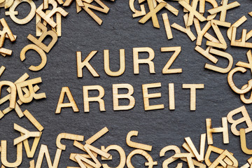 Text Kurzarbeit aus Holzbuchstaben auf Schieferplatte