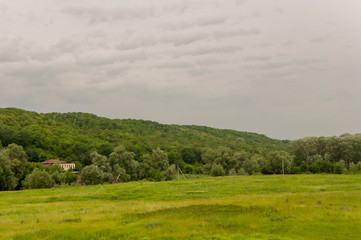 Suburb and villages. Big mountains and green forests. Trees and their shadows on the grass. Summer day with dark blue and grey sky and  clouds. Fields. Fresh air.