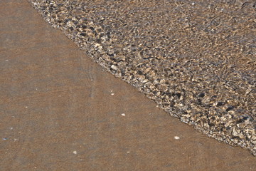 Eine Meeres Welle kommt sehr langsam und schneidet das Bild in zwei Dreiecke. Eine Hälfte hat einen Wellenmuster, von der Sonne beleuchtet und mit kleinen Schatten Textur. Die andere Hälfte hat noch 