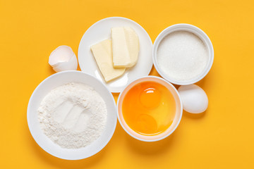 Ingredients for baking on an orange background, top view, minimal style. Flour, eggs, sugar and butter in white bowls. Cooking and baking concept, flat lay