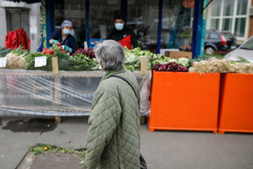  Senior woman walks by a street vegetable market during the covid-19 lockdown.