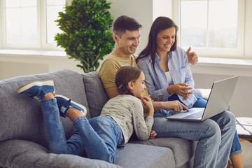 Happy family looking at a laptop while sitting comfortably on a sofa in a living room at the...