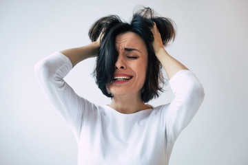 Bipolar disorder. Portrait of a young woman in white clothes who is crying while touching her head...