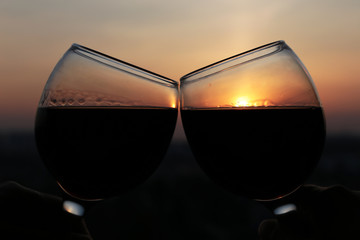 Two glasses with red wine on colorful sunset background. Couple clink glasses, concept of celebration, romantic evening at home quarantine, love date