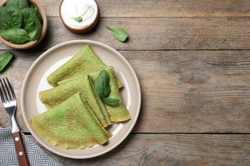 Delicious spinach crepes served on wooden table, flat lay. Space for text