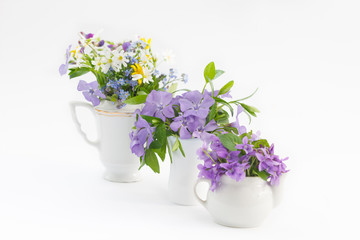 Wild  flowers in three small vases on white background. Beautiful spring forest flowers.