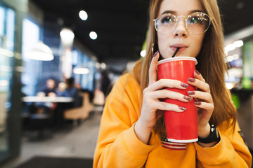 Closeup photo, attractive girl drinking cola tubes from red glass at fast food restaurant, looking...