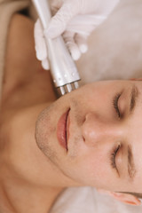 Obraz na płótnie Canvas Vertical shot of a handsome man enjoying skincare treatment by professional dermatologist. Rf-lifting concept