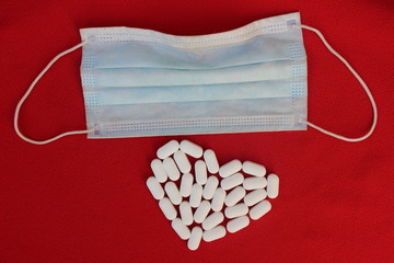 Blue protective medical mask on a red background and a heart made of pills. Medical protection...