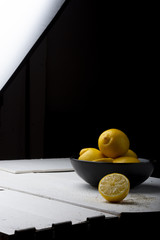 Yellow lemons in a black bowl, on a white wooden table.