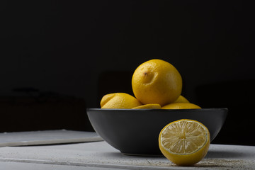 Yellow lemons in a black bowl, on a white wooden table.