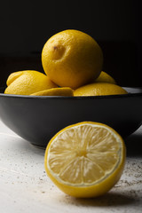 Yellow lemons in a black bowl, on a white wooden table.