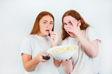 two redheaded scared women look frightened one with remote control another with popcorn standing on isolated white backgroung, leisure time concept