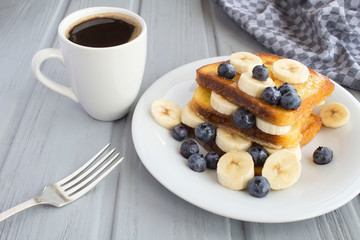 Breakfast: french toasts with blueberries, banana,honey and coffee on the  grey wooden background. Closeup.