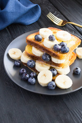 French toasts with blueberries, banana  and honey  in the black  plate on the dark wooden background. Location vertical.