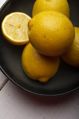 Yellow lemons in a black bowl, on a white wooden table.