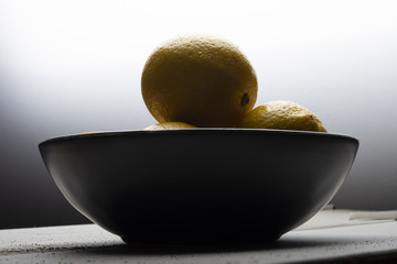 Yellow lemons in a black bowl, on a white wooden table.