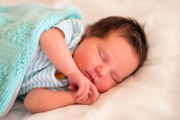 Obraz na płótnie Canvas Little newborn baby in striped shirt sleeping in bed under woolen blanket. Portrait of calm infant child with closed eyes laying on side under turquoise knitted blanket. Children day sleep concept