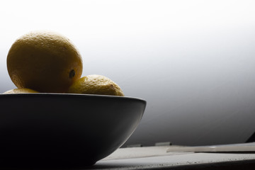 Yellow lemons in a black bowl, on a white wooden table.