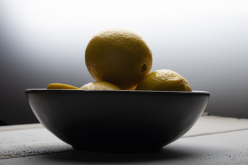 Yellow lemons in a black bowl, on a white wooden table.