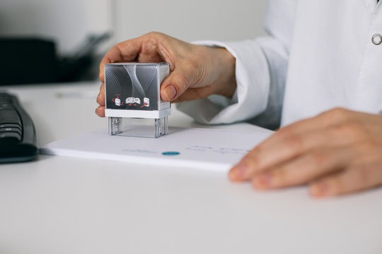 Close-up of doctor stamping a prescription at desk in medical practice