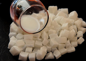 Milk in a glass on coconut cubes on black background. Coconut dried fruit. Candied coconut. Coconut...
