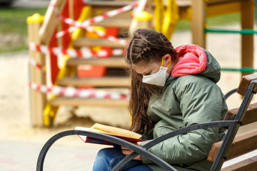 Obraz premium A masked teenage girl is reading a book in the playground.