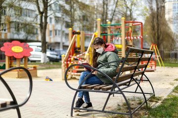Fototapeta na wymiar A masked teenage girl is reading a book in the playground.