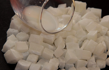 Milk in a glass on coconut cubes on black background. Coconut dried fruit. Candied coconut. Coconut...