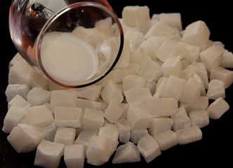 Milk in a glass on coconut cubes on black background. Coconut dried fruit. Candied coconut. Coconut...