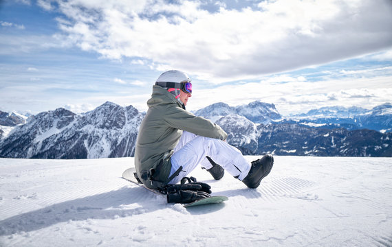 Smiling woman sitting with snowboard on viewpoint and enjoying view at distance