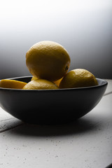 Yellow lemons in a black bowl, on a white wooden table.