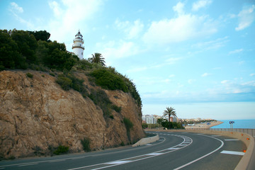 Turn of the road near the lighthouse in the tourist town. The lighthouse stands at the highest point of the city. Around it is a road and a view of the sandy beach.