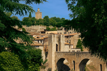 View of the municipality of Besalu. You can see the bridge, gate and tower through the branches of trees.