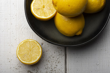 Yellow lemons in a black bowl, on a white wooden table.