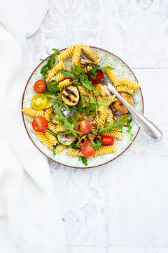 Plate of vegetarian pasta salad with grilled zucchini, tomatoes, arugula, red onions and balsamic vinegar