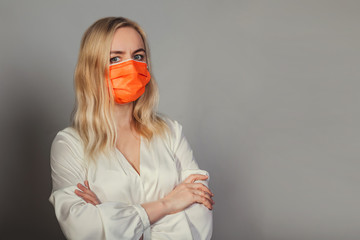 A woman with an anxious face and an orange medical mask crossed her arms over her chest. Office...