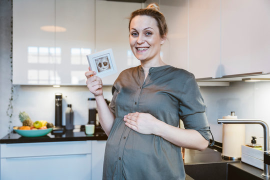 Portrait of pregnant woman in kitchen at home holding ultrasound image