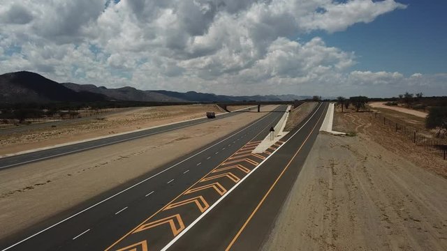 4K aerial video of newly upgraded main A1/B1 highway outside Windhoek to town Okahandja with bush covered mountains, dry endless savanna view, metal silo towers in Khomas Region, central Namibia