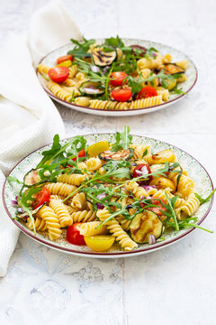 Two plates of vegetarian pasta salad with grilled zucchini, tomatoes, arugula, red onions and balsamic vinegar