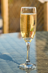 Close up view of a single flute glass of champagne on the glass table top of garden furniture