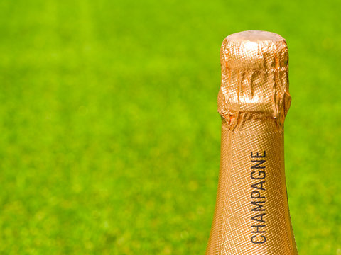 Gold foil covered top of an unopened bottle champagne against a plain green background. Space for copy left.