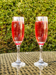 Pink champagne in two flute glasses side by side on a glass table top in a garden