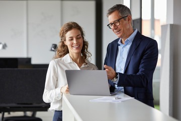 Smiling businessman and businesswoman working together on laptop in office