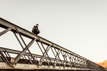 Man crouching on metal bar of an old railway bridge