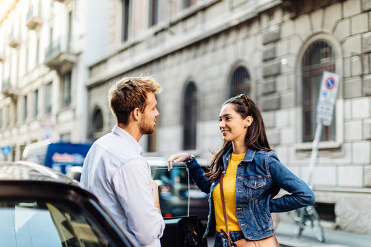 Young couple talking at a car in the city, Milan, Italy
