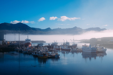 Fototapeta premium fishing boats on a pier in blue fog in an early sunny morning in the summer